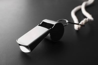 Photo of Referee whistle with cord on black textured table, closeup