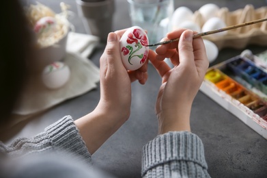 Photo of Woman painting Easter egg at black table, closeup