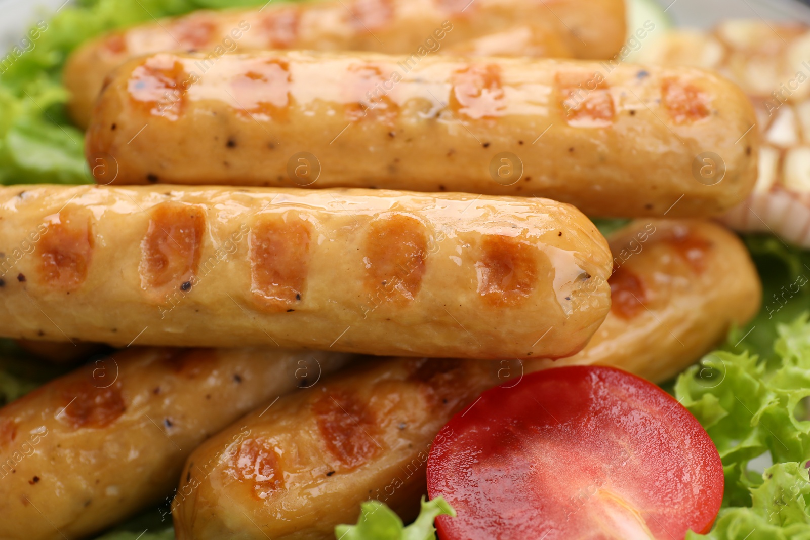 Photo of Delicious grilled vegan sausages with fresh lettuce and tomato as background, closeup