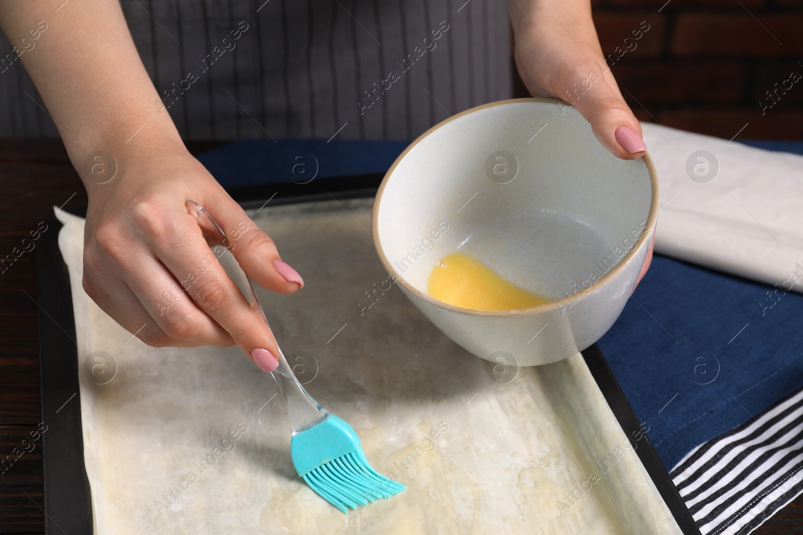 Photo of Making delicious baklava. Woman buttering dough at table, closeup