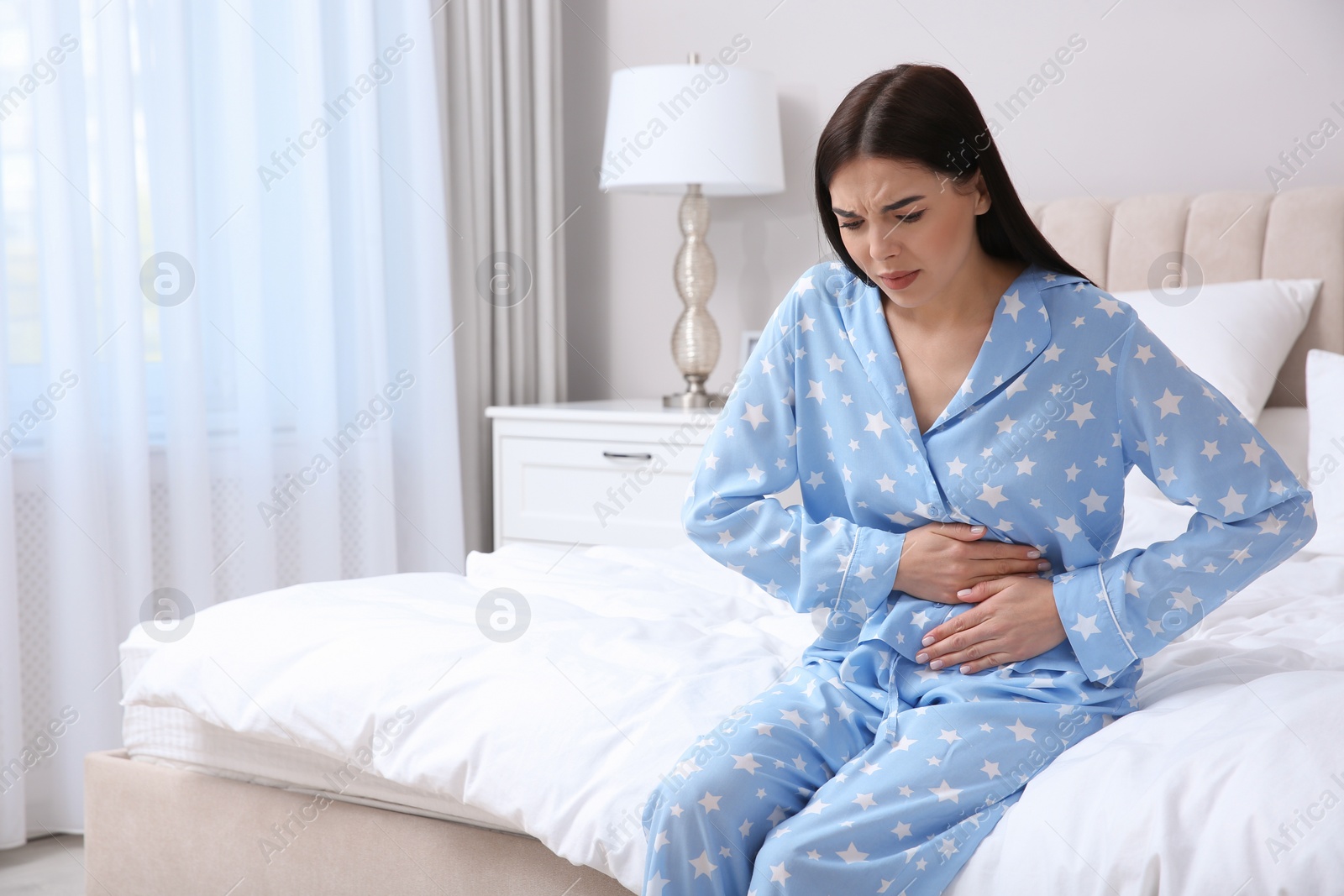 Photo of Young woman suffering from stomach ache in bedroom