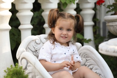 Photo of Cute little girl in white dress sitting in chair outdoors