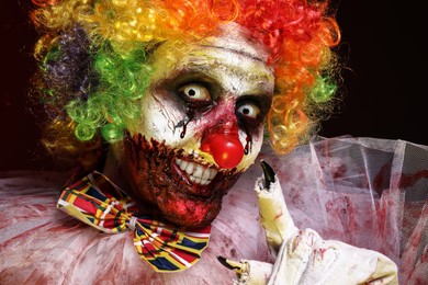 Photo of Portrait of terrifying clown on black background, closeup. Halloween party costume