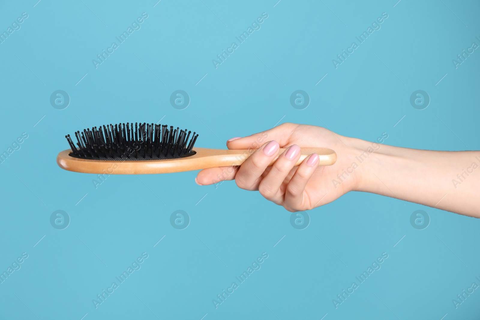 Photo of Woman holding wooden hair brush against blue background, closeup