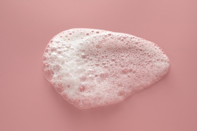 Photo of Spot of white washing foam on pale pink background, top view