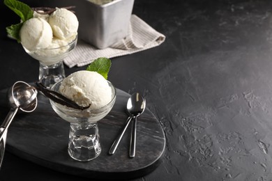 Photo of Tasty ice cream with vanilla pods in glass dessert bowls on black table. Space for text