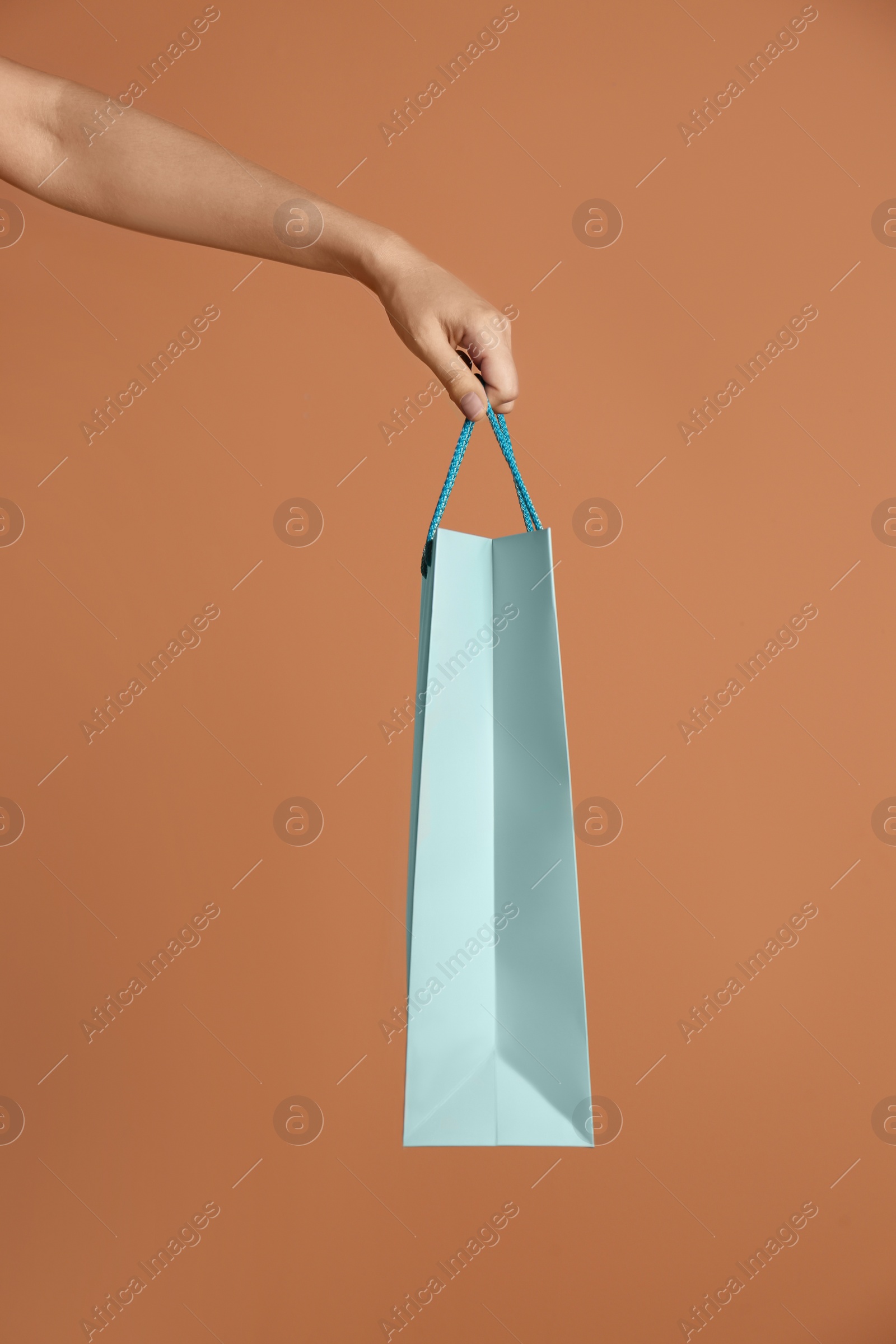 Photo of Woman holding paper shopping bag on light brown background, closeup