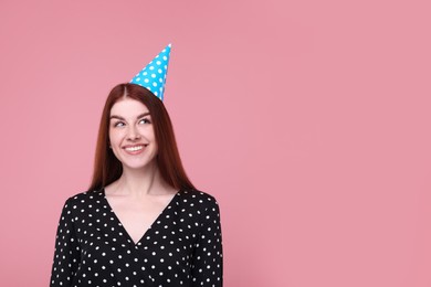 Happy woman in party hat on pink background, space for text