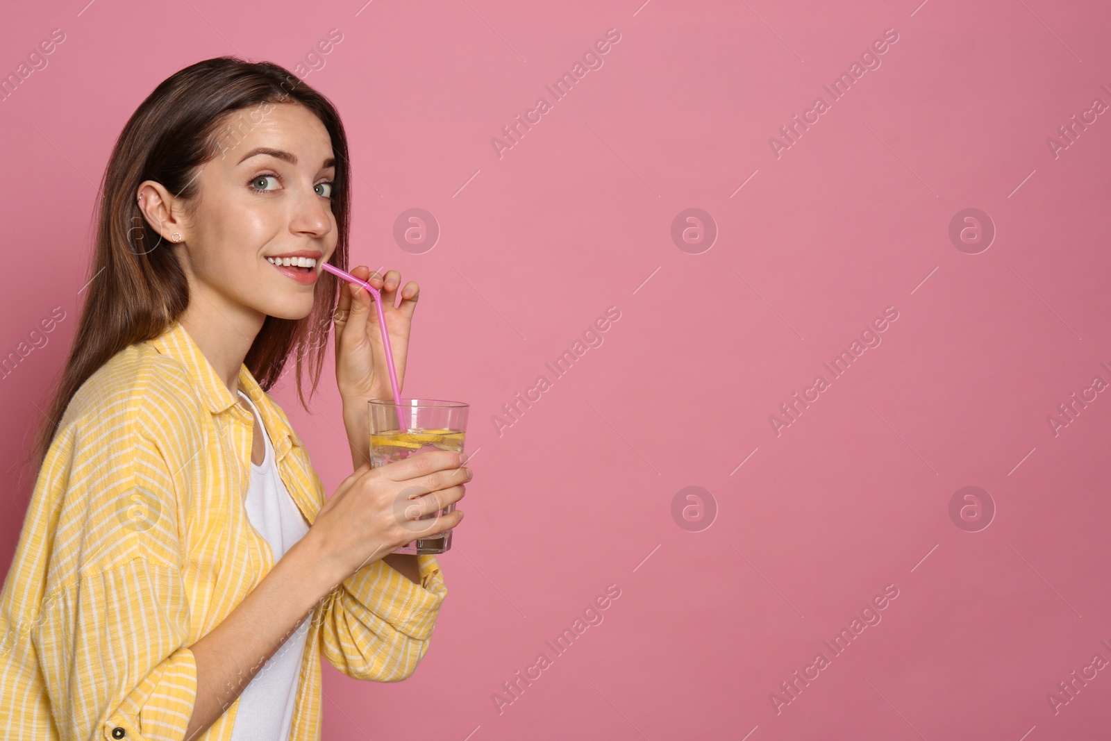 Photo of Young woman drinking lemon water on pink background. Space for text