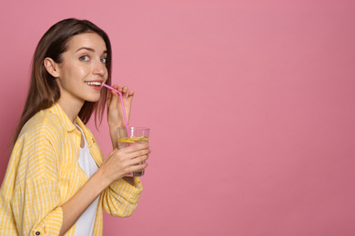 Photo of Young woman drinking lemon water on pink background. Space for text