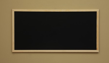 Photo of Clean black chalkboard hanging on beige wall