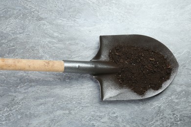 Photo of Metal shovel with fertile soil on gray textured surface, top view