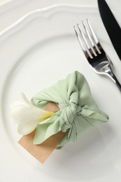 Photo of Furoshiki technique. Gift packed in green fabric with flower and blank card on plate, top view