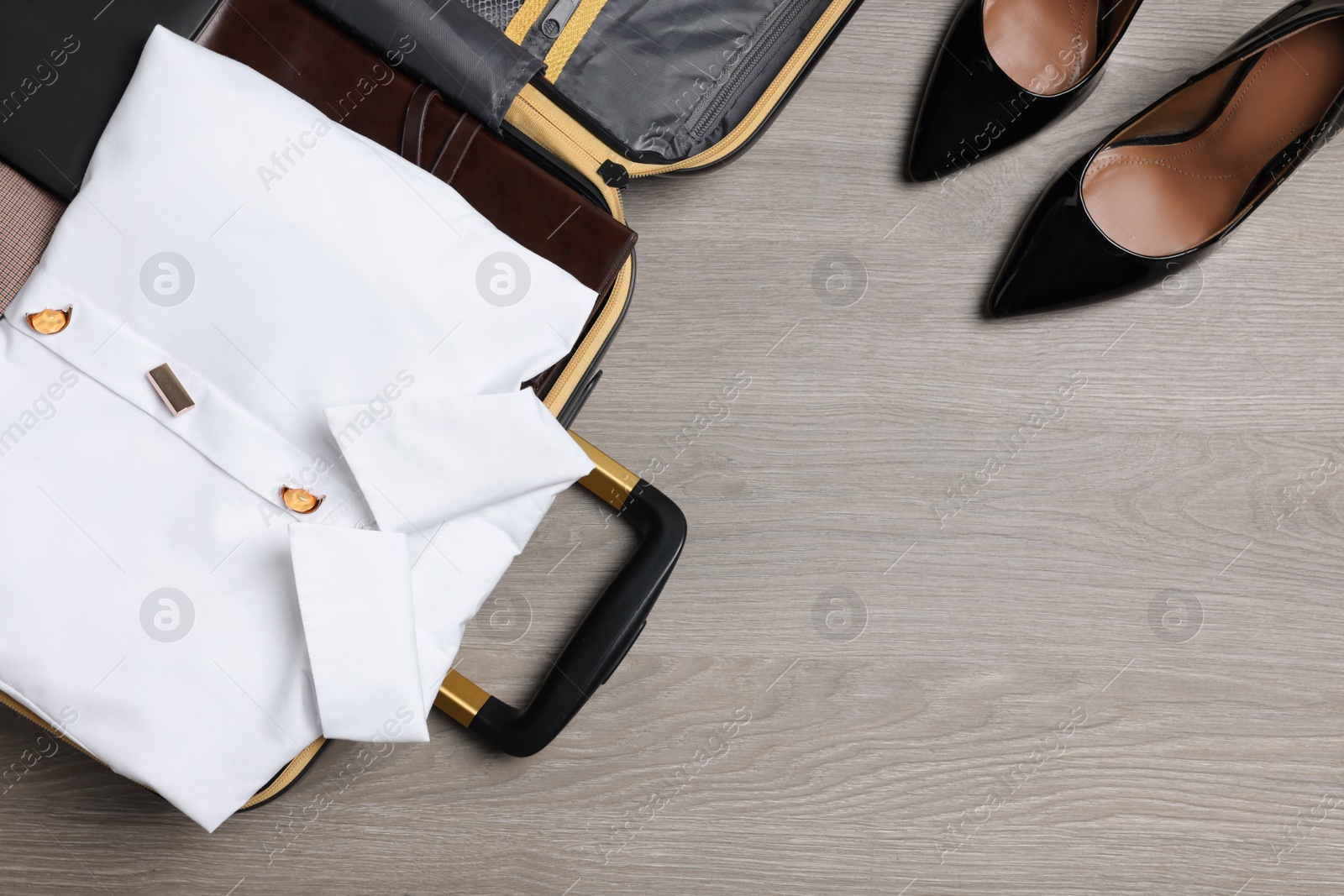 Photo of Open suitcase, clothes and shoes on wooden background, flat lay with space for text. Business trip preparations