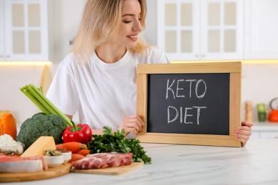 Photo of Woman holding blackboard with phrase Keto Diet at white table in kitchen, closeup