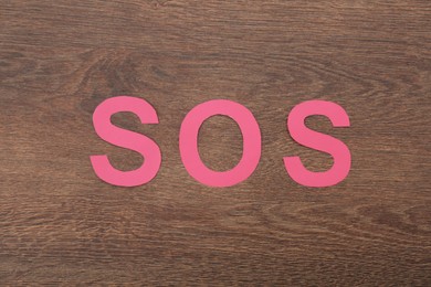 Photo of Abbreviation SOS made of paper letters on wooden background, top view