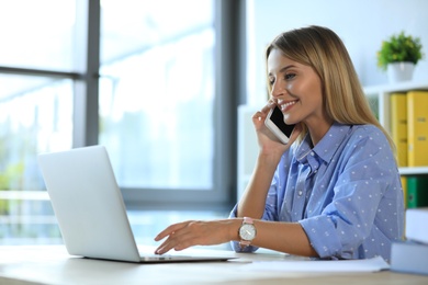 Photo of Female business trainer talking on phone while working with laptop in office