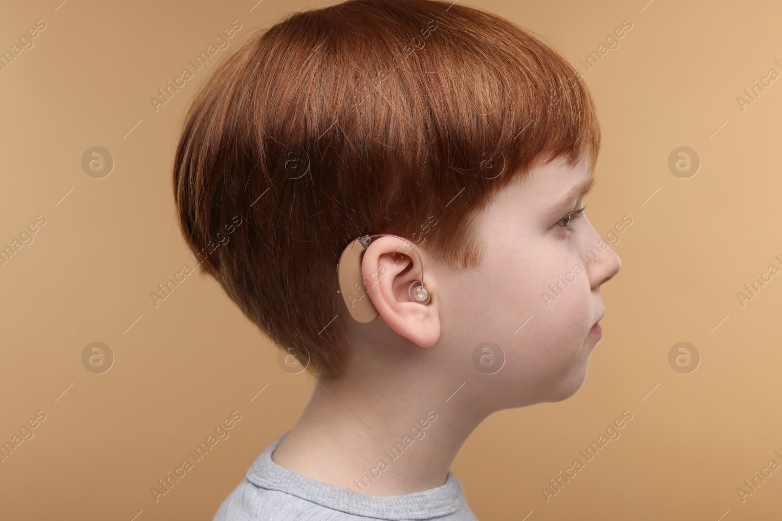 Photo of Little boy with hearing aid on pale brown background