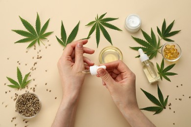 Photo of Woman applying CBD oil or THC tincture on skin at beige background, top view