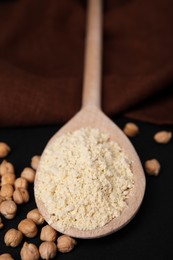 Spoon with chickpea flour and seeds on black table, closeup