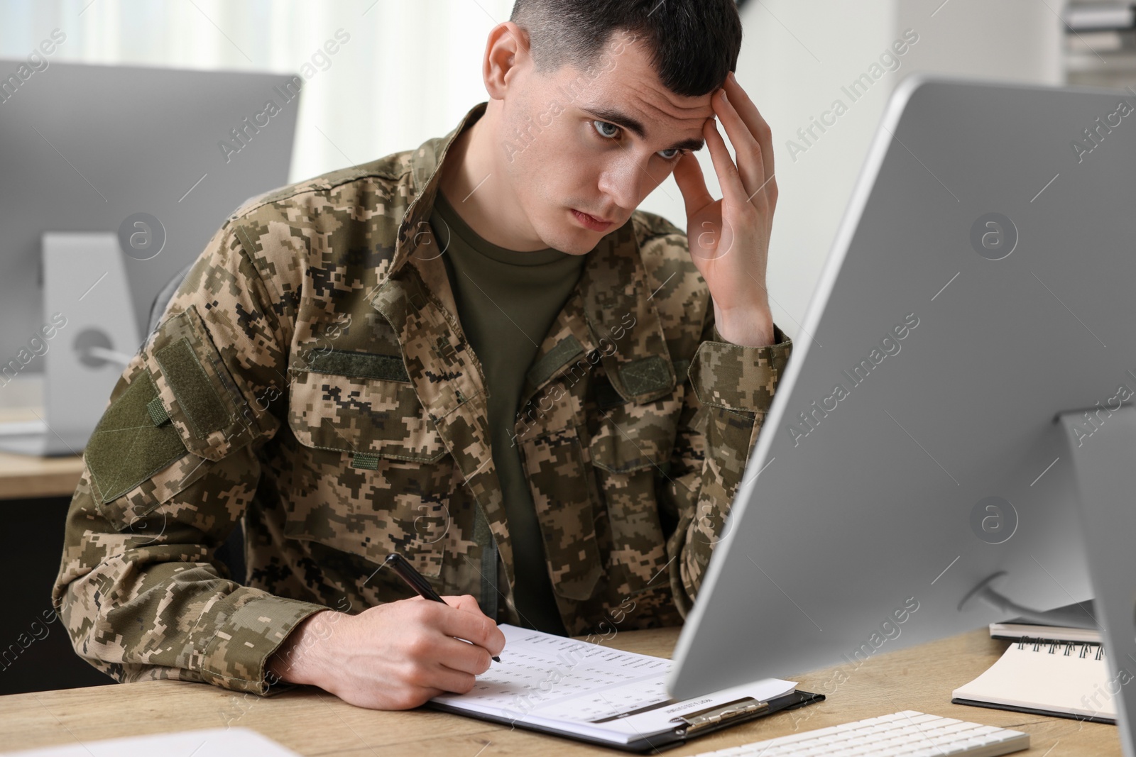 Photo of Military service. Young soldier working at wooden table in office