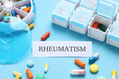 Photo of Card with word Rheumatism and pills on light blue background