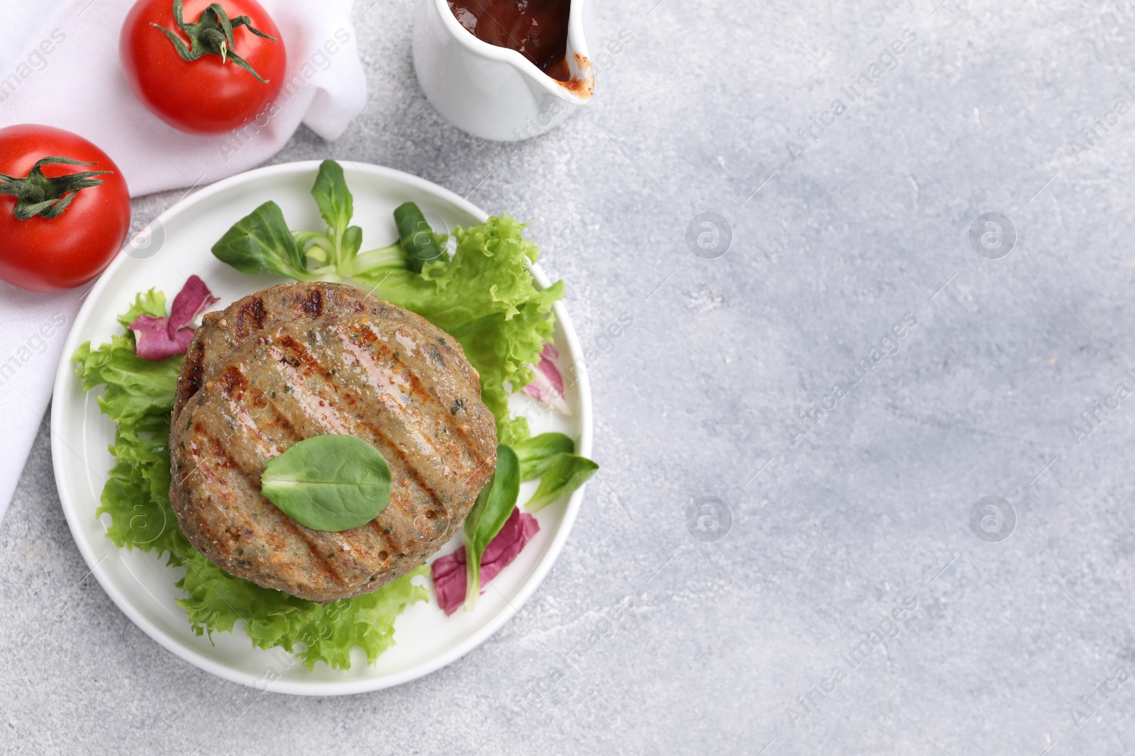 Photo of Delicious grilled vegan cutlets, lettuce, spinach and tomatoes on light grey table, flat lay. Space for text