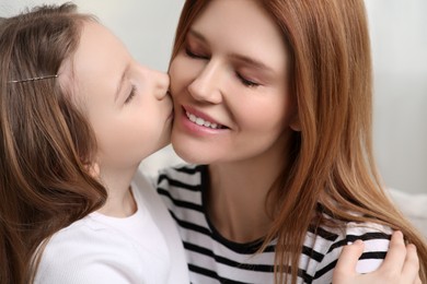 Cute daughter kissing her mom at home, closeup