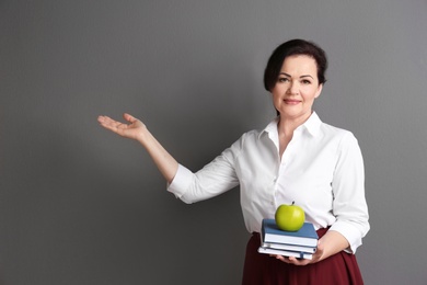 Portrait of female teacher with notebooks and apple on grey background