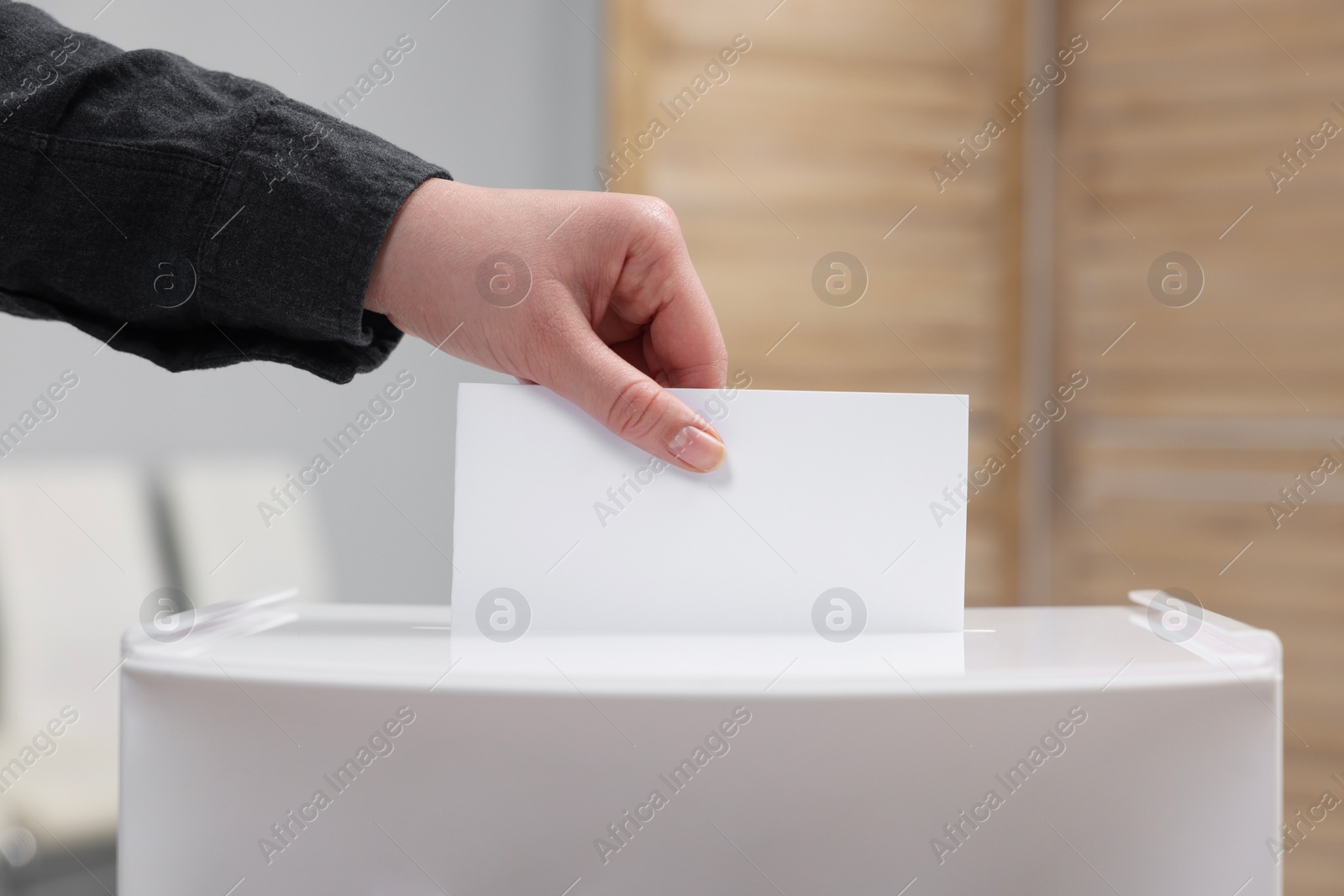 Photo of Woman putting her vote into ballot box on blurred background, closeup