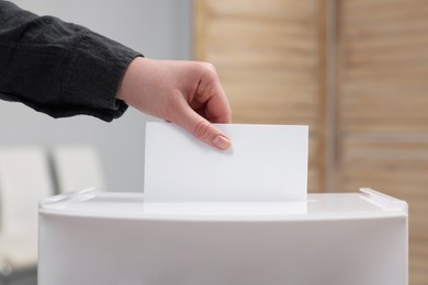 Photo of Woman putting her vote into ballot box on blurred background, closeup