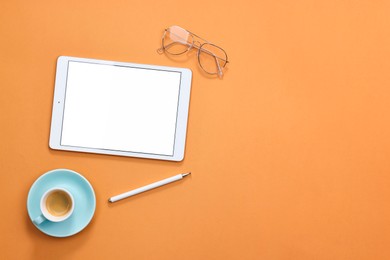 Photo of Modern tablet, glasses, stylus and cup of coffee on orange background, flat lay. Space for text