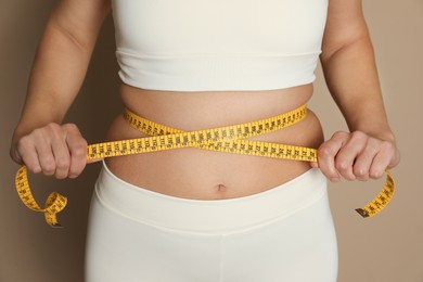 Photo of Woman measuring waist with tape on beige background, closeup