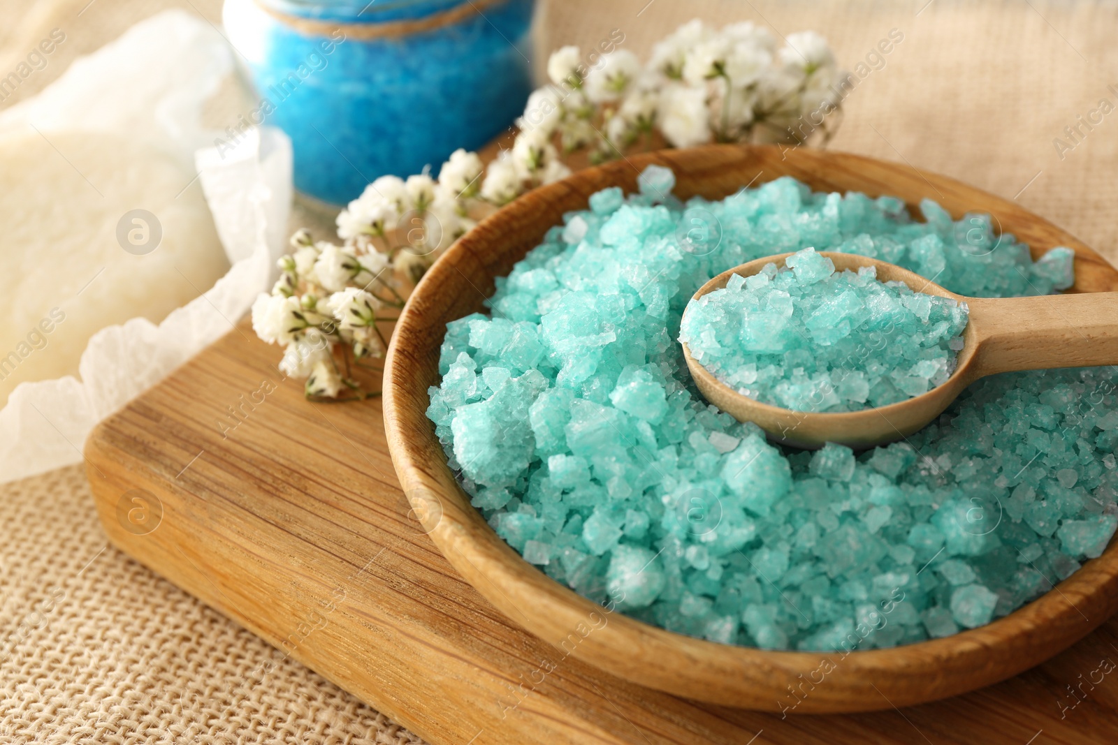 Photo of Turquoise sea salt and beautiful flowers on table, closeup