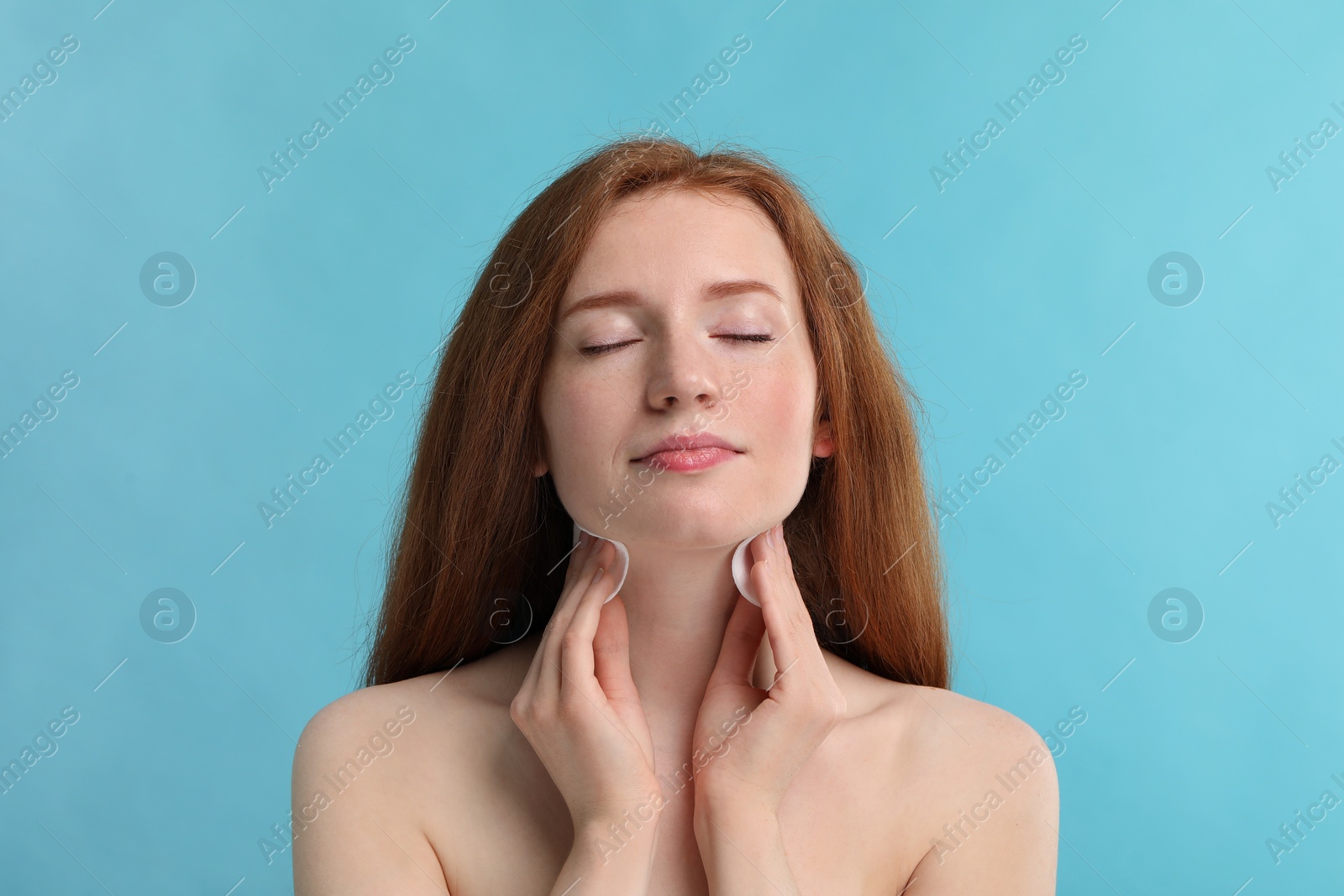 Photo of Beautiful woman with freckles wiping neck on light blue background