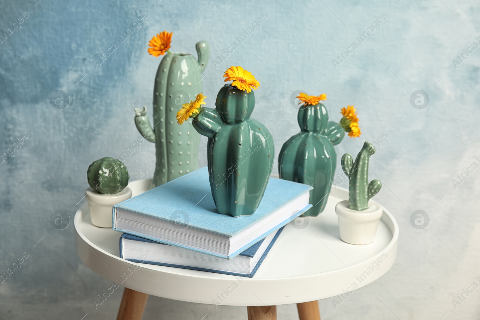 Photo of Trendy cactus shaped vases and books on table against color background. Creative decor