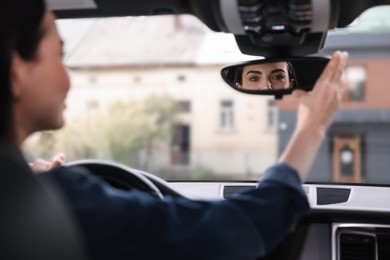 Woman adjusting rear view mirror inside her car, closeup