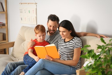 Photo of Happy family reading book together on sofa in living room at home