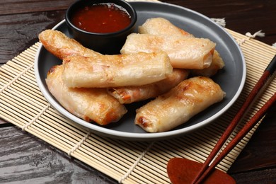 Photo of Tasty fried spring rolls and sauce served on wooden table, closeup