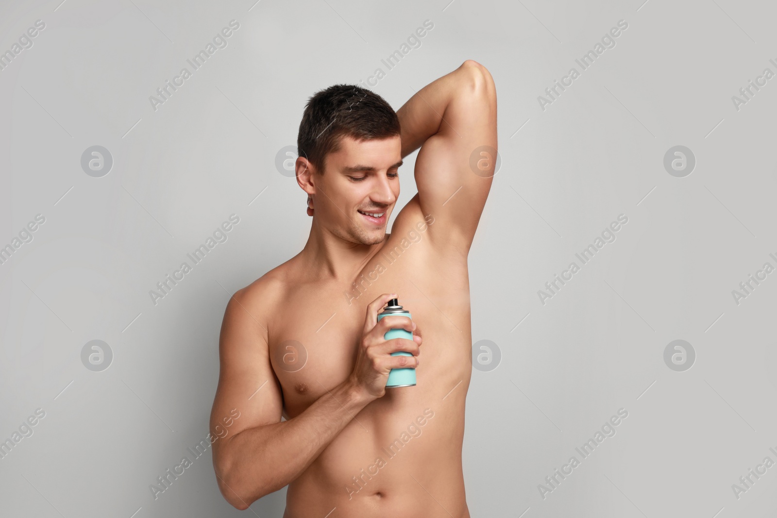 Photo of Young man applying deodorant to armpit on light background