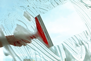 Photo of Woman cleaning window with squeegee on spring day, closeup