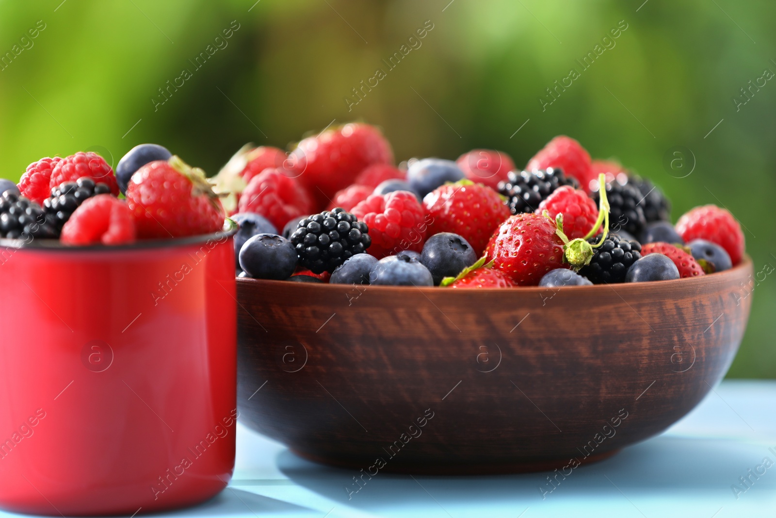 Different fresh ripe berries on light blue table outdoors Photo of Different fresh ripe berries on light blue table outdoors