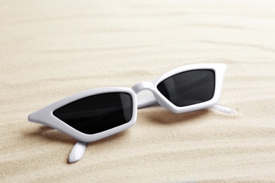 Stylish sunglasses on white sand. Summer time