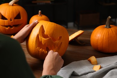 Woman carving pumpkin for Halloween at wooden table, closeup. Space for text