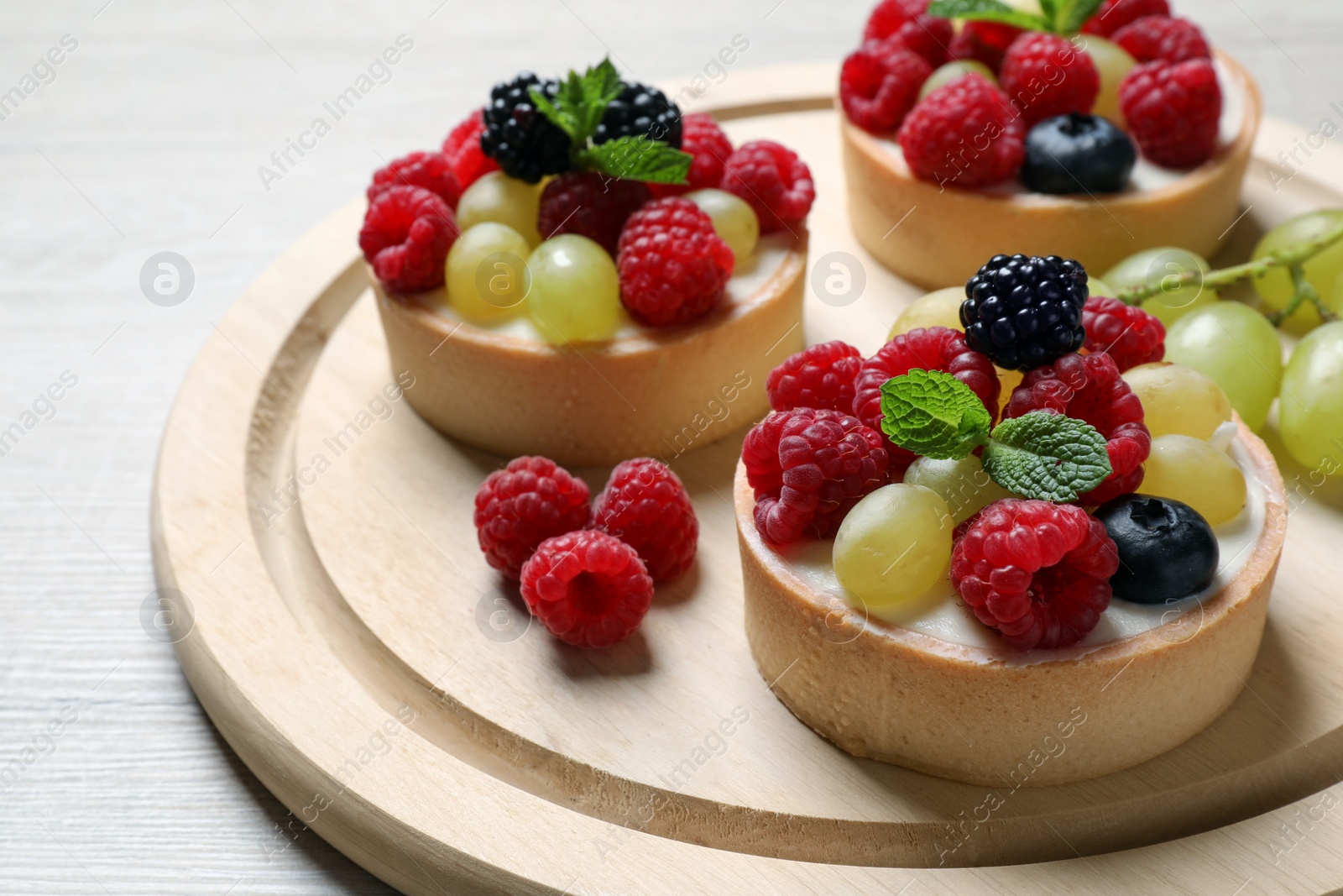 Photo of Delicious tartlets with berries on light wooden table, closeup