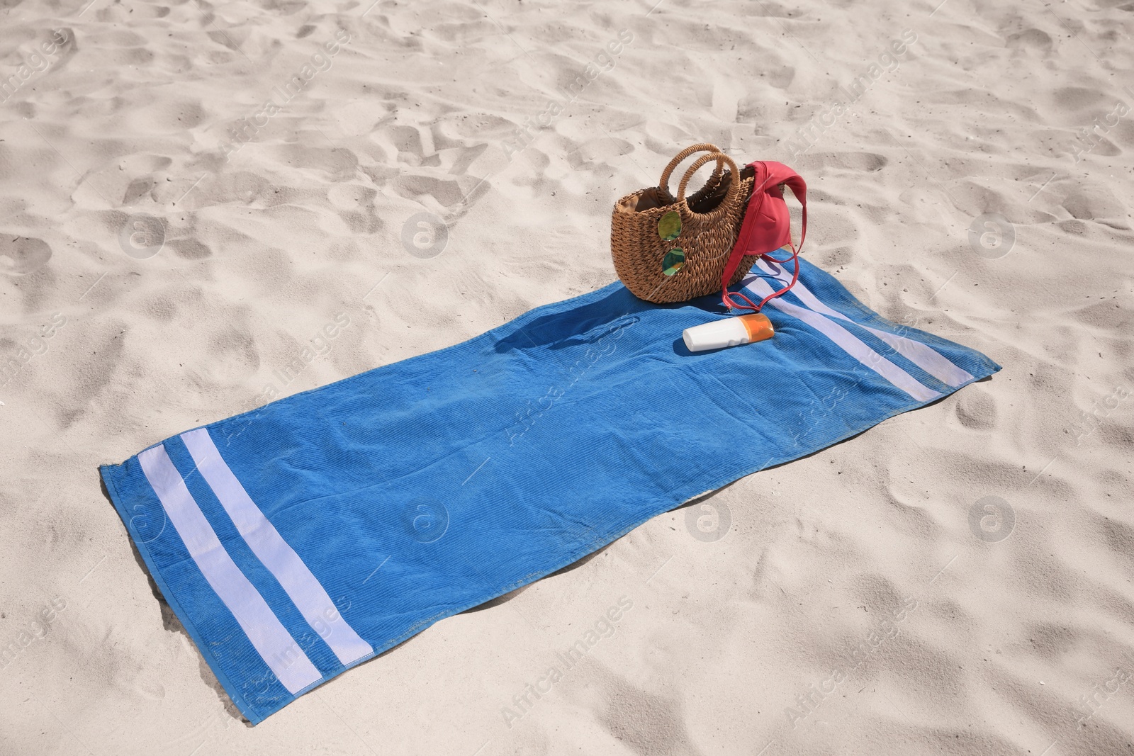 Photo of Blue striped beach towel with bag, swimsuit and accessories on sand
