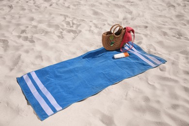 Photo of Blue striped beach towel with bag, swimsuit and accessories on sand
