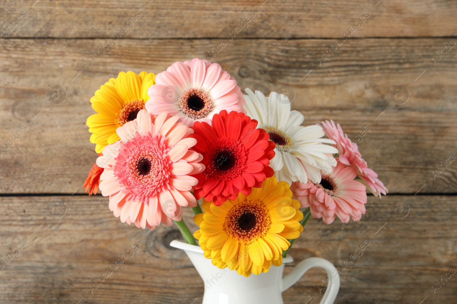 Photo of Bouquet of beautiful colorful gerbera flowers in vase on wooden background