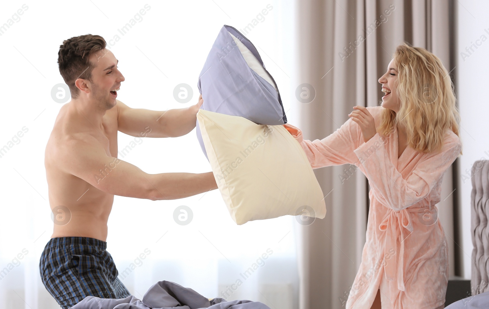 Photo of Lovely young couple having pillow fight on bed at home