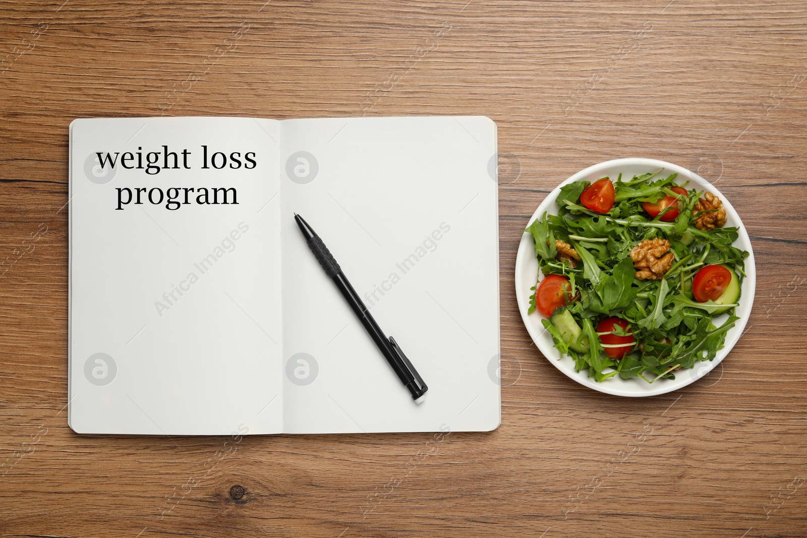 Photo of Weight loss concept. Open notebook with pen and bowl of salad on wooden table, flat lay